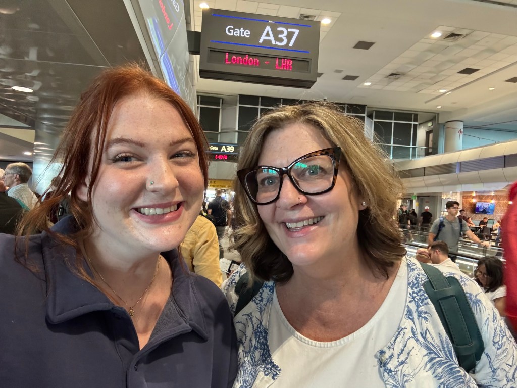 Josie and Chelsea at DIA under the gate sign displaying LONDON as the destination.